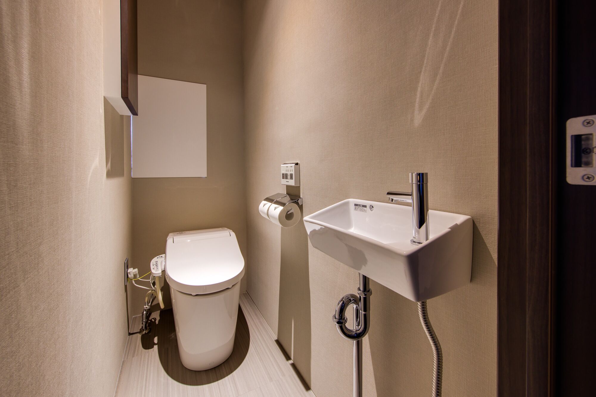 A compact bathroom with a toilet, a wall-mounted sink, and a toilet paper holder.