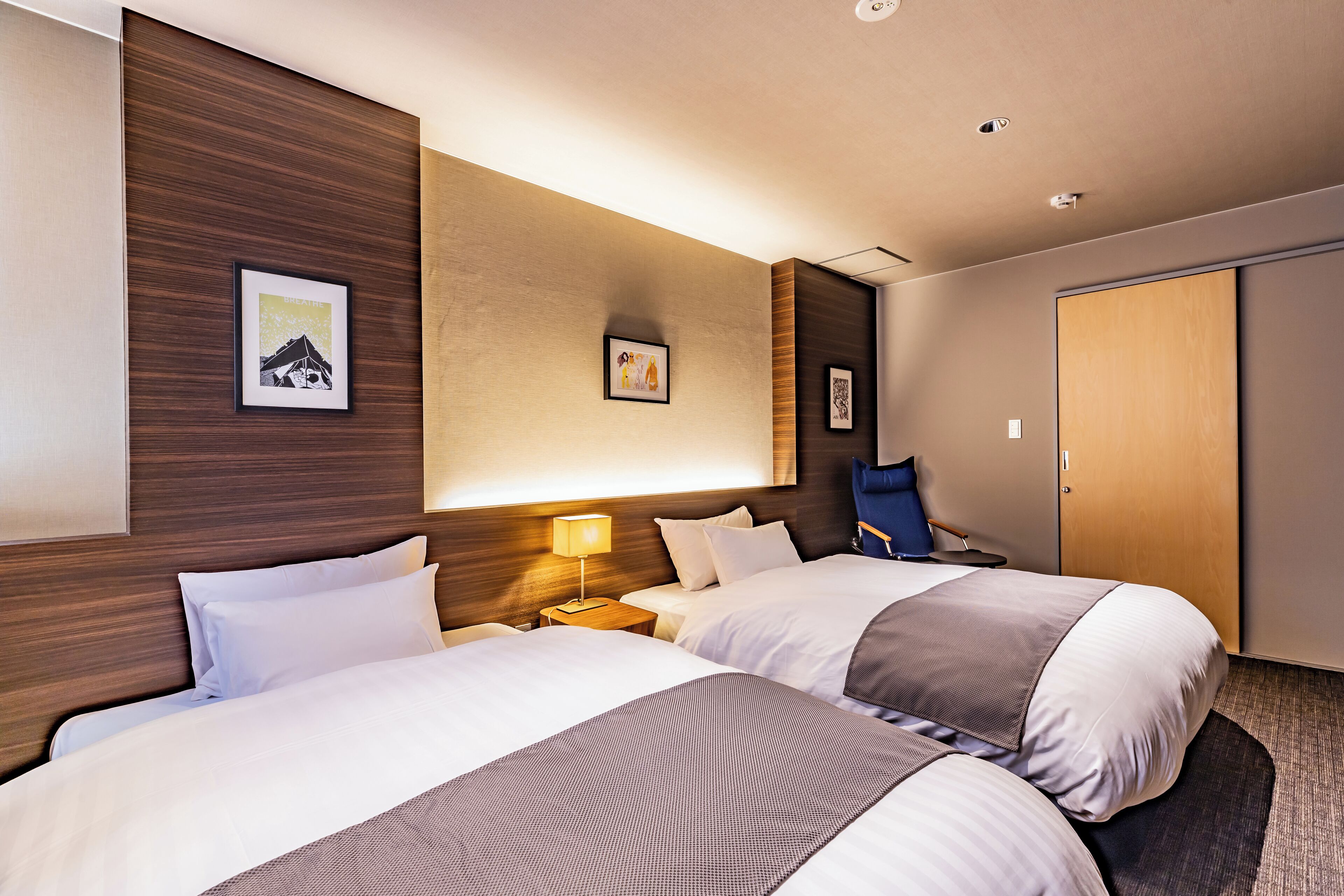 Habitación de hotel con dos camas, cabecero de madera, lámpara de pared y una puerta.