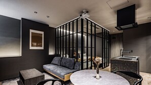 Una sala de estar moderna con un sofá gris, una mesa redonda con un florero, un taburete de madera y una silla negra.