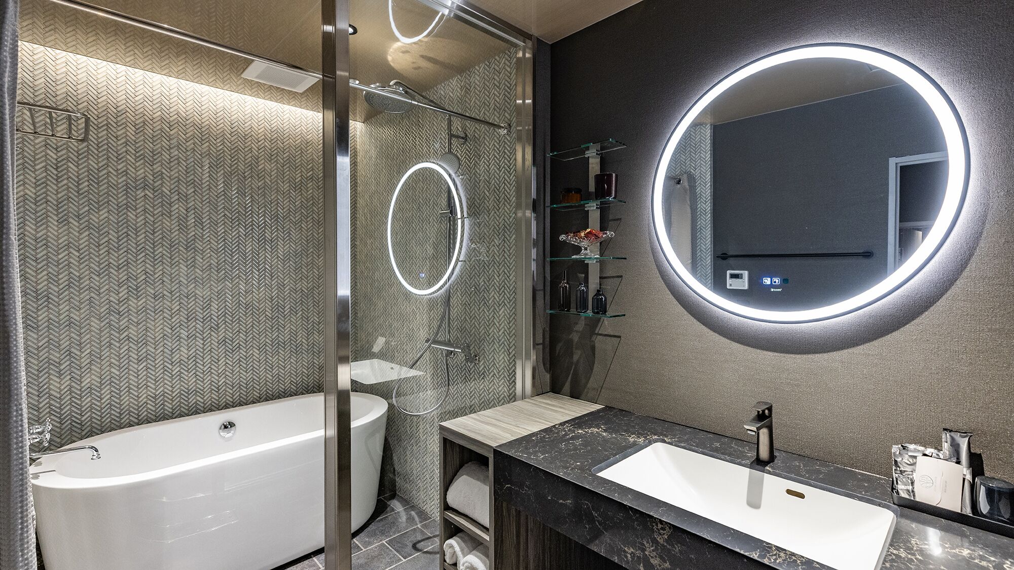A modern bathroom with a freestanding bathtub, a vanity with a large mirror, and a shower area with a circular light.