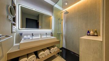 A modern bathroom with a large mirror, two sinks, a shower, and a shelf with toiletries.