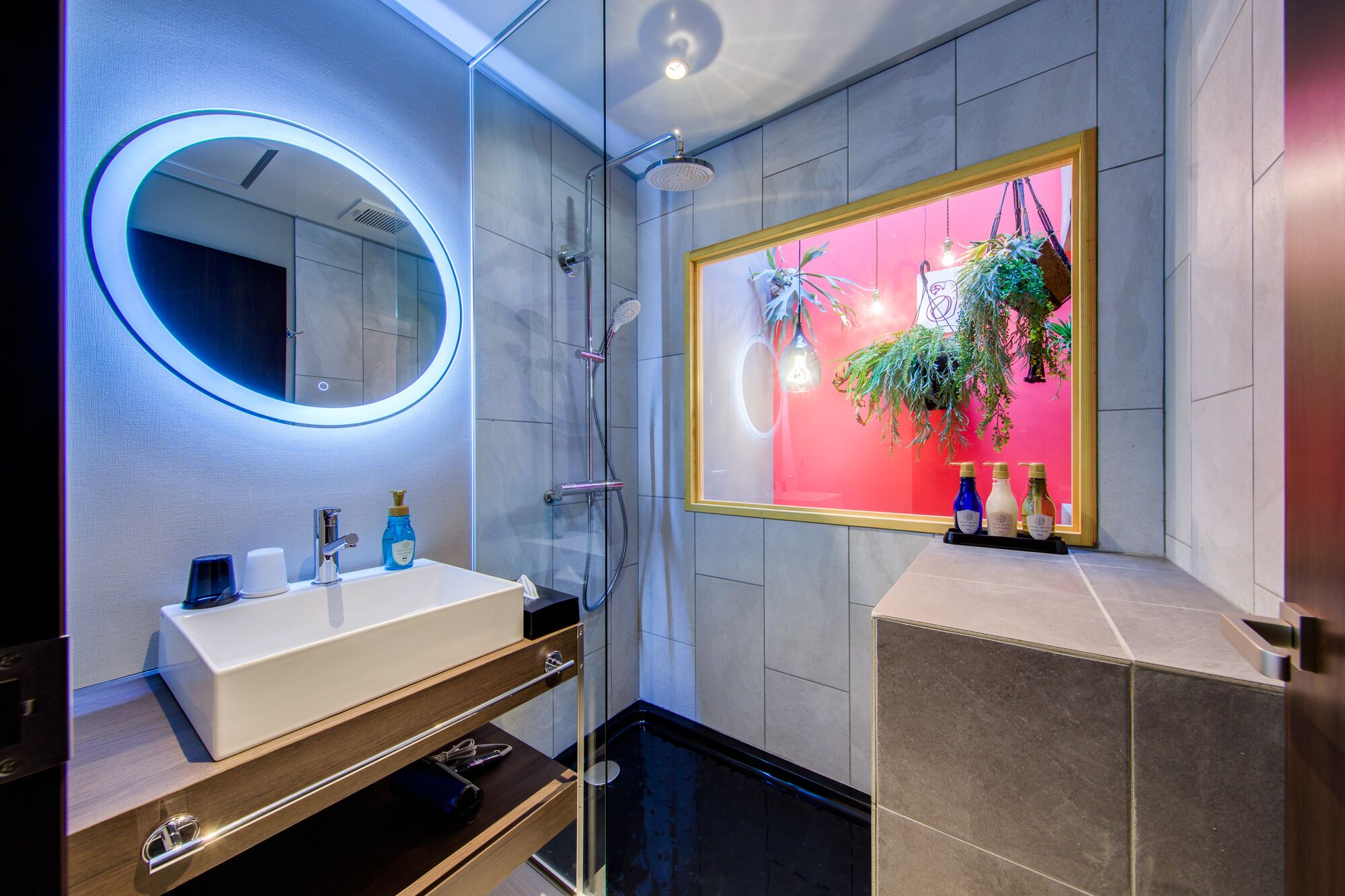 Un baño moderno con un espejo redondo, cerramiento de ducha de vidrio y un tocador con lavabo y espacio de almacenamiento.