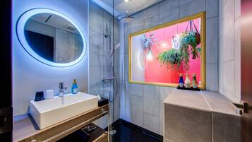 Un baño moderno con un espejo redondo, cerramiento de ducha de vidrio y un tocador con lavabo y espacio de almacenamiento.