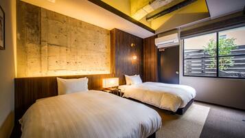 A modern hotel room with two beds, a large textured wall, a window with a view of greenery, and a ceiling with exposed beams.