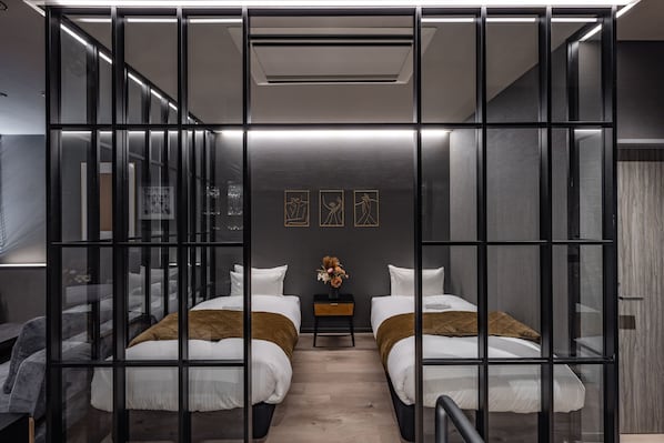 Habitación de hotel moderna con dos camas, una mesita con un florero y vistas a la ciudad a través de amplias ventanas.