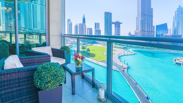 A balcony with wicker furniture, a vase with flowers, and a view of a city skyline and water body. - Elite Royal Apartment - Burj Khalifa & Fountain view - Opal (Dubai)