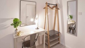 A modern bedroom with a white bed, a bedside table, a mirror, and a window.