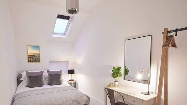 A bedroom with a bed, desk, chair, and a skylight.
