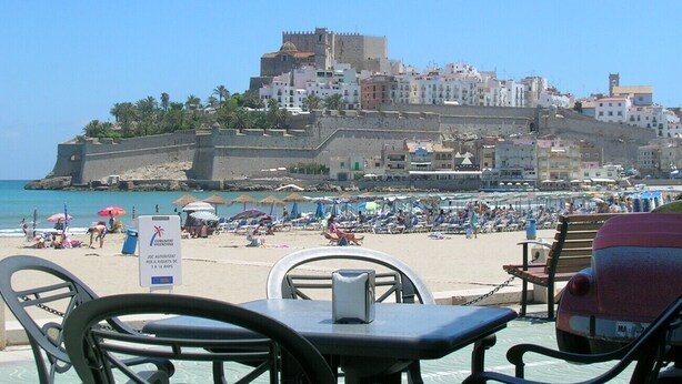 A beach with a historic castle in the background, a sign indicating a 14-year-old minimum, and beach umbrellas. - Les Doyes Bl 3 1-36  LEK (Peñiscola)