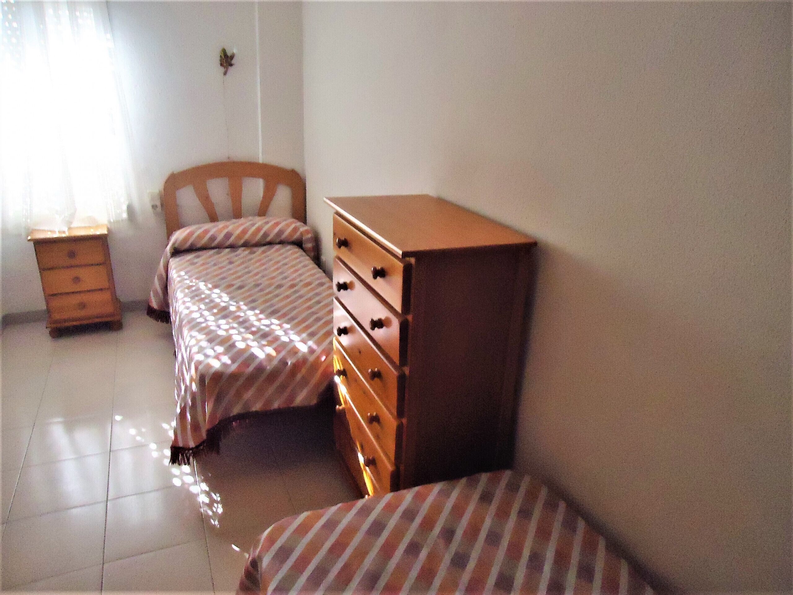 A bedroom with two single beds, a wooden dresser, and a nightstand.