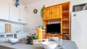 Keittiössä on valkoiset kaapit, puinen kaappi, jossa on televisio, sekä ruokapöytä, jonka päällä on kulhoja, laseja ja hedelmäkori.