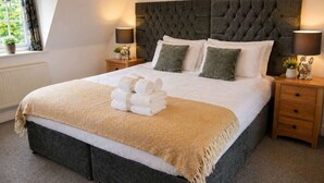 A large bed with a tufted headboard, two bedside tables with lamps, and a window with curtains. - Measure Cottage - Sleeps up to 4 - Henley in Arden - HOT TUB (Henley-in-Arden)