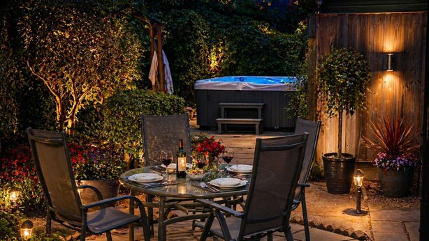 An outdoor patio with a table set for dining, surrounded by chairs, potted plants, and a hot tub in the background. - Measure Cottage - Sleeps up to 4 - Henley in Arden - HOT TUB (Henley-in-Arden)