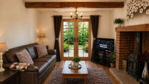 A cozy living room with a leather sofa, a coffee table, a fireplace, and a TV. - Measure Cottage - Sleeps up to 4 - Henley in Arden - HOT TUB (Henley-in-Arden)