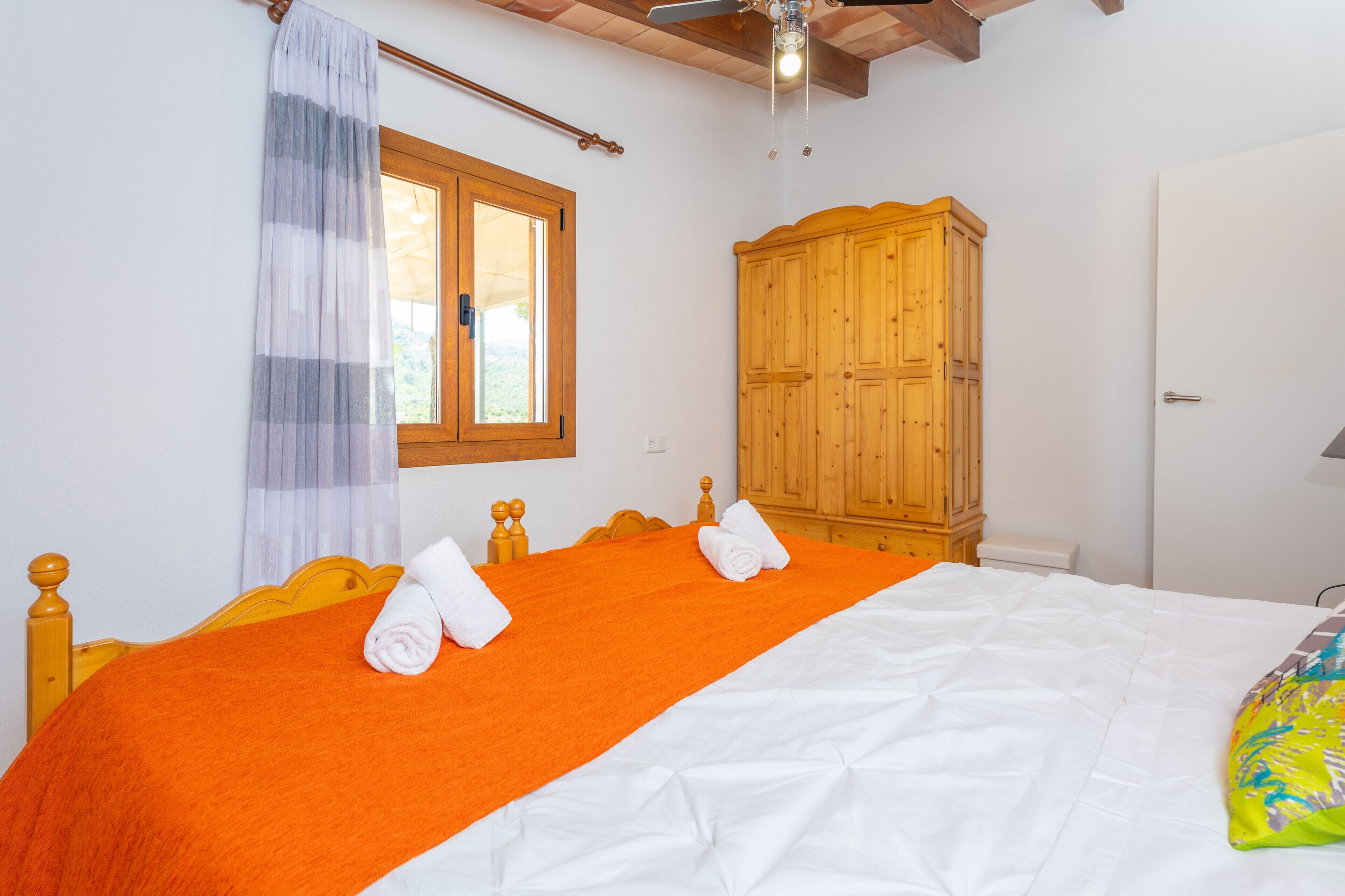 A hotel room with a bed, wooden wardrobe, and a window with curtains.
