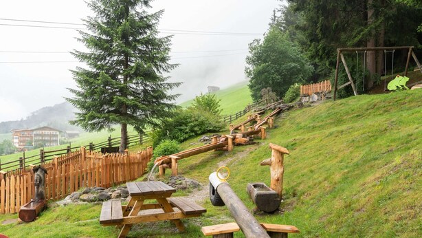 A playground with wooden structures, including a slide and swings, set against a backdrop of trees and a hill. - Quaint Apartment in Hainzenberg near Horbergbahn (Hainzenberg)
