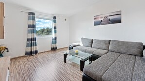 A modern living room with a grey sofa, a glass coffee table, and a view of a pier through a window. - Simplistic Apartment in Vir With Garden (Vir)