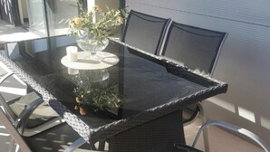 Una mesa con cubierta de vidrio, sillas de mimbre, un florero con flores y una vela sobre una mesa redonda.