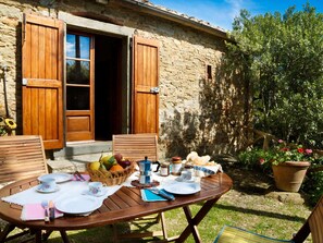 An outdoor dining area with a table set for two, a basket of fruit, and a coffee machine. - Elegant 2-bedroom Holiday Home in Tuscan (Cortona)