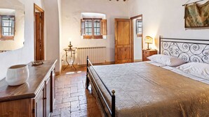 Ein Schlafzimmer mit Holzboden, einem Bett mit Metallkopfteil, einem Heizkörper und einem Fenster mit geöffneten Rollläden.