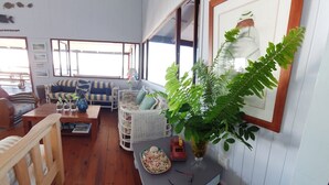Una sala de estar acogedora con piso de madera, un sofá azul y blanco a rayas, un sillón de mimbre blanco, una mesita con una planta y un cuadro en la pared.