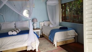 Un dormitorio con dos camas, cada una con dosel, una mesita de noche con lámpara y vistas al exterior a través de una ventana.