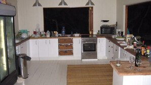 Een keuken met witte kastjes, een fornuis, een magnetron en een groot raam.
