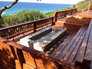 A wooden deck with built-in seating and a small water feature, overlooking a body of water and greenery. - Mar Azul 14 (Ponta d'Ouro)