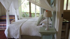 Ein Schlafzimmer mit Baldachinbett, Nachttisch mit Lampe und Blick ins Freie.