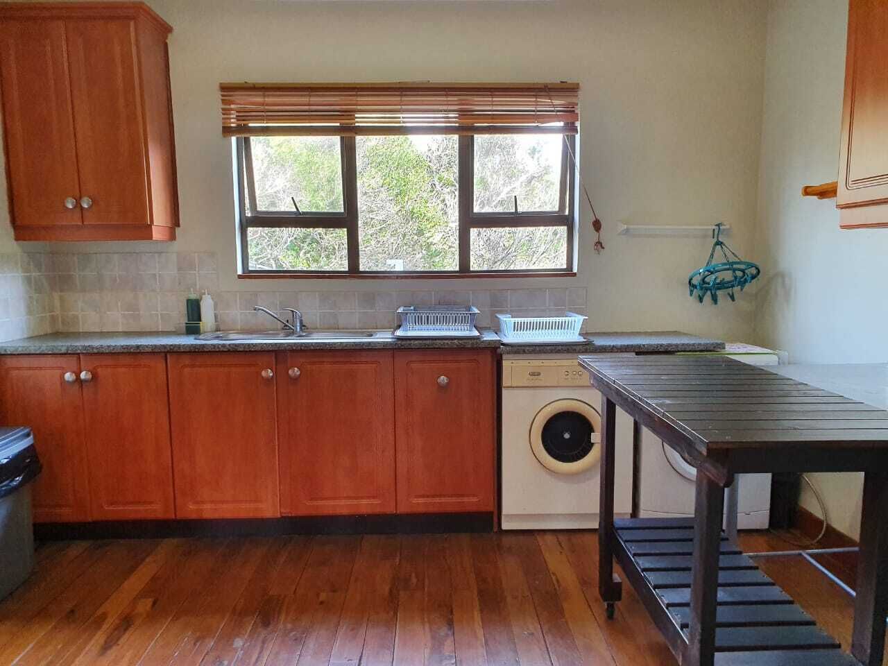 A kitchen with wooden cabinets, a washing machine, a window with blinds, and a table.