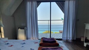 A bedroom with a large bed, a wooden floor, and a view of the sea through a glass door. - Mar Azul 18 (Ponta d'Ouro)