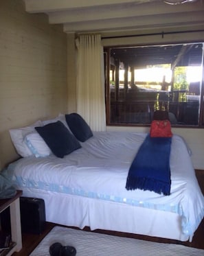 Un letto con biancheria bianca e dettagli blu, una coperta rossa e una finestra con vista su mobili da esterno.