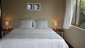 A bedroom with a large bed, two bedside lamps, and two framed pictures on the wall. - Mar Azul 1B (Ponta d'Ouro)