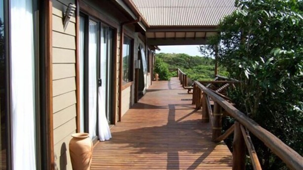 A wooden deck with a railing, leading to a building with large windows and a tiled roof. - Mar Azul 26 (Ponta d'Ouro)