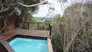 A wooden deck with a swimming pool, surrounded by dense vegetation and a view of the landscape. - Mar Azul 26 (Ponta d'Ouro)