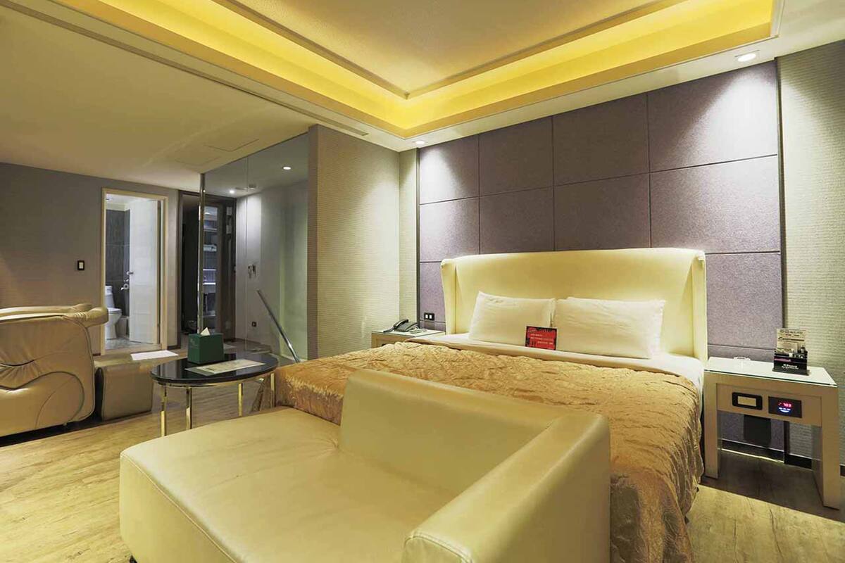 Ein modernes Hotelzimmer mit einem großen Bett, einer Sitzecke mit einem Sessel, einem kleinen Tisch und einem Nachttisch mit einer Lampe.
