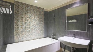 A modern bathroom with a large bathtub, a sink, and a tiled shower wall.