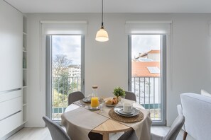 Een moderne eetruimte met een ronde tafel, stoelen en een stadszicht door grote ramen.