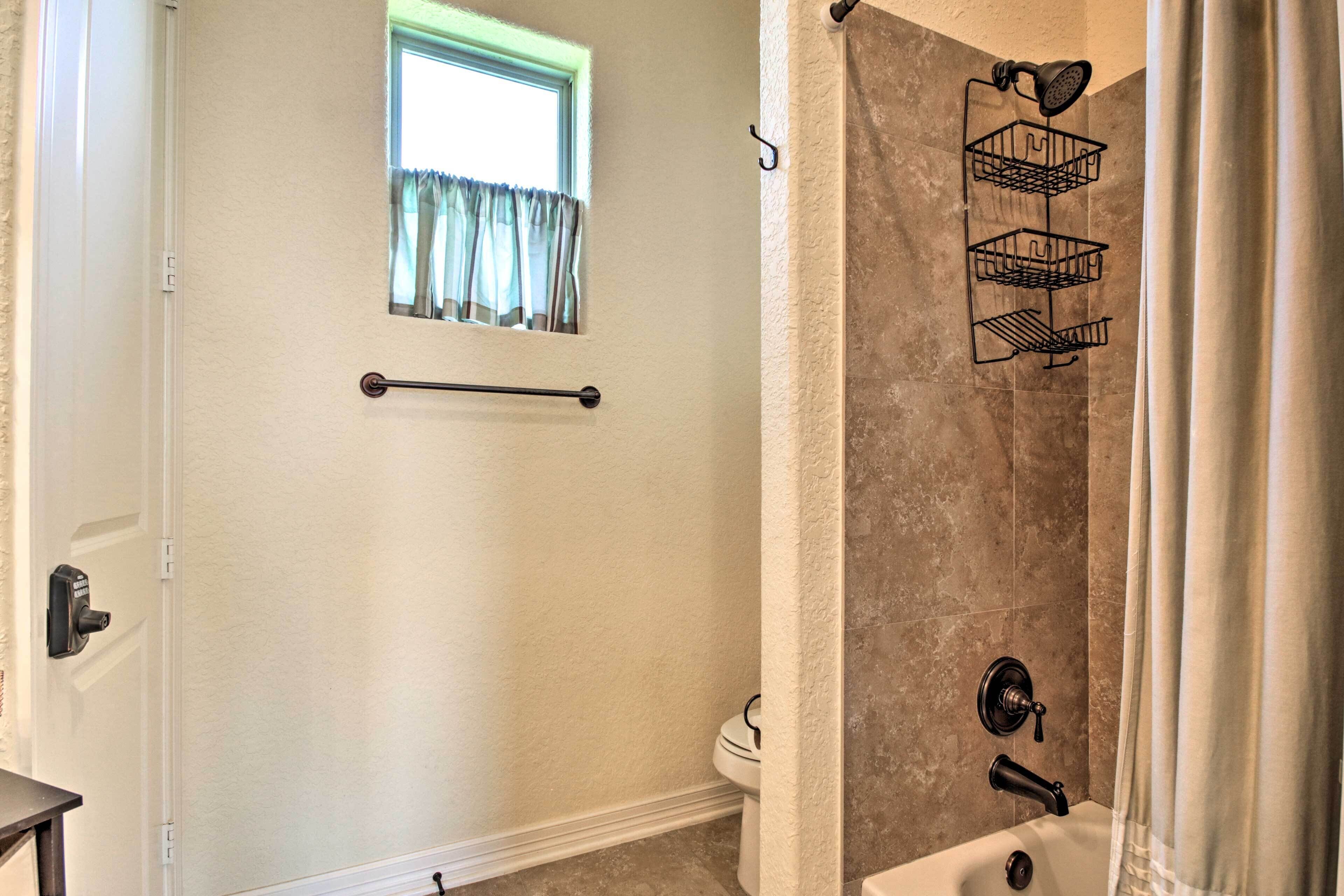 A bathroom with a shower, a window with curtains, a towel rack, and a toilet.