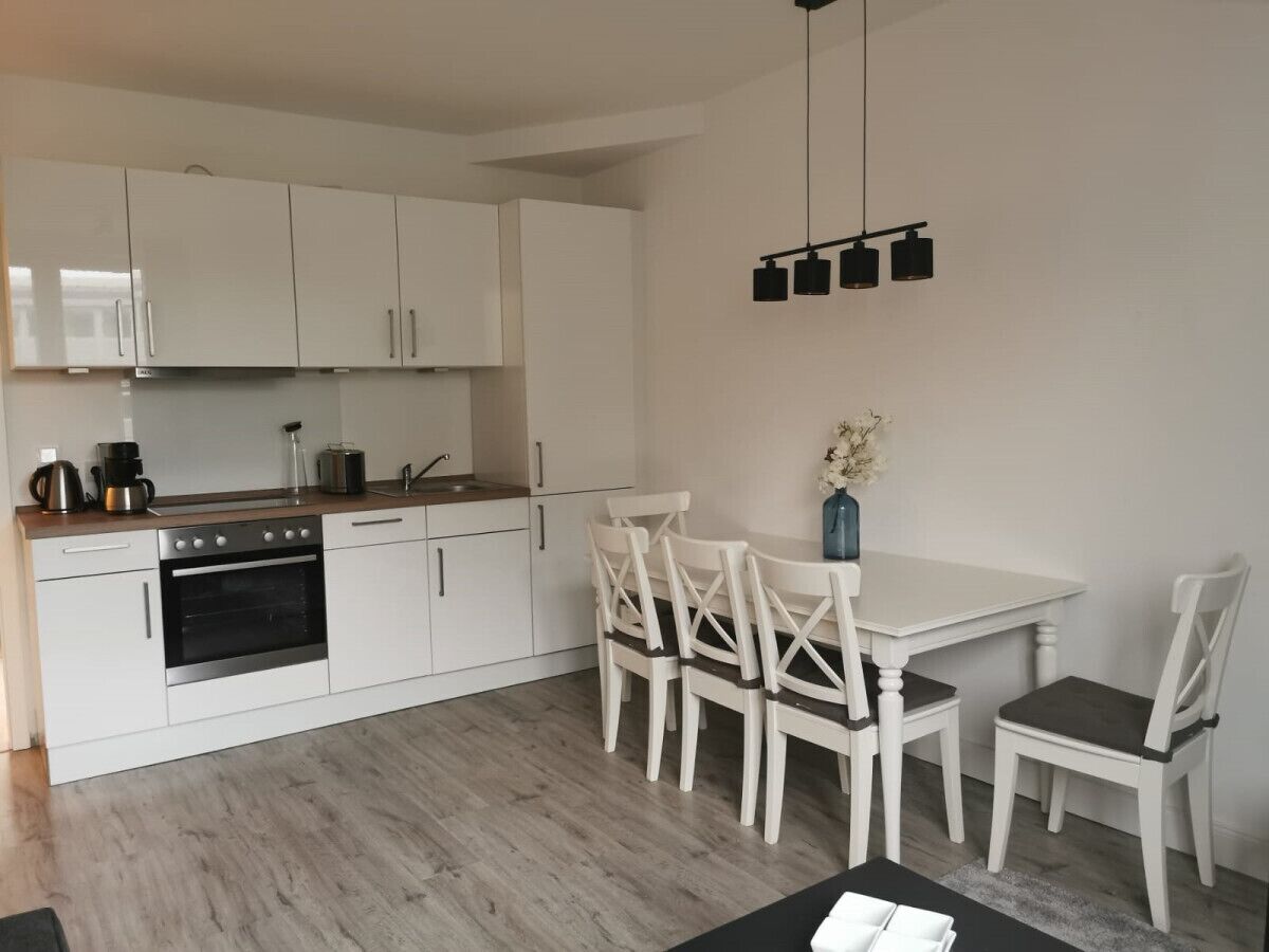 Una cocina moderna con armarios blancos, horno integrado y una zona de comedor con sillas y mesa blancos.