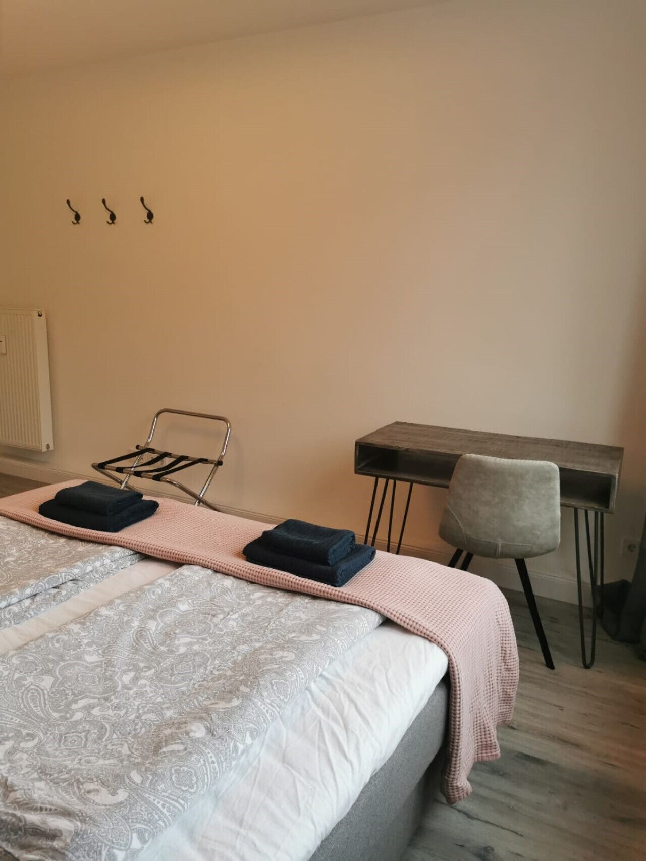 Ein Schlafzimmer mit einem Bett, einem Schreibtisch und einem Stuhl. Handtücher liegen auf dem Bett und eine Heizung ist an der Wand angebracht.
