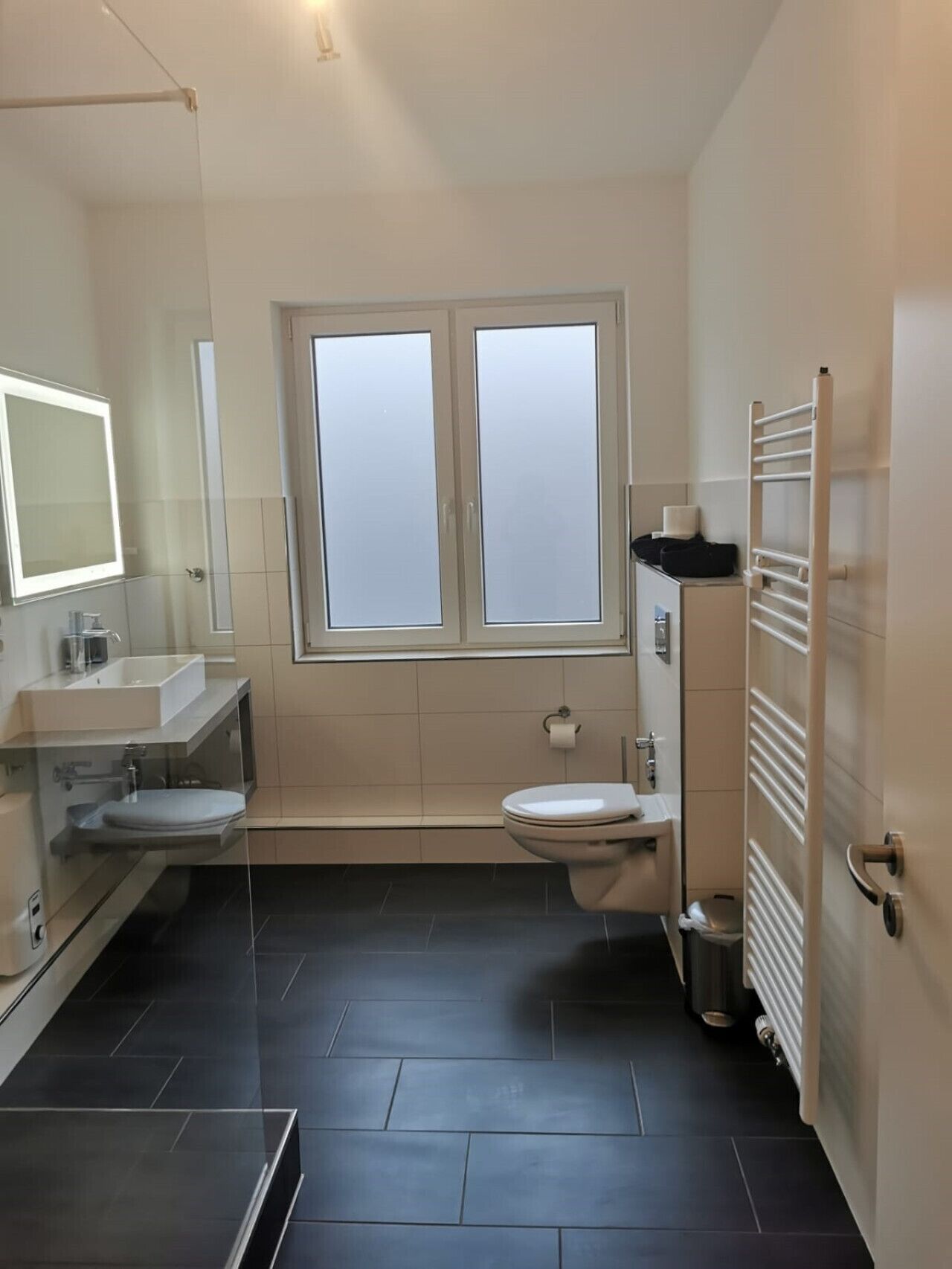 Ein modernes Badezimmer mit Duschkabine, einem Doppelwaschbecken mit Spiegel, Toilette und Handtuchhalter.