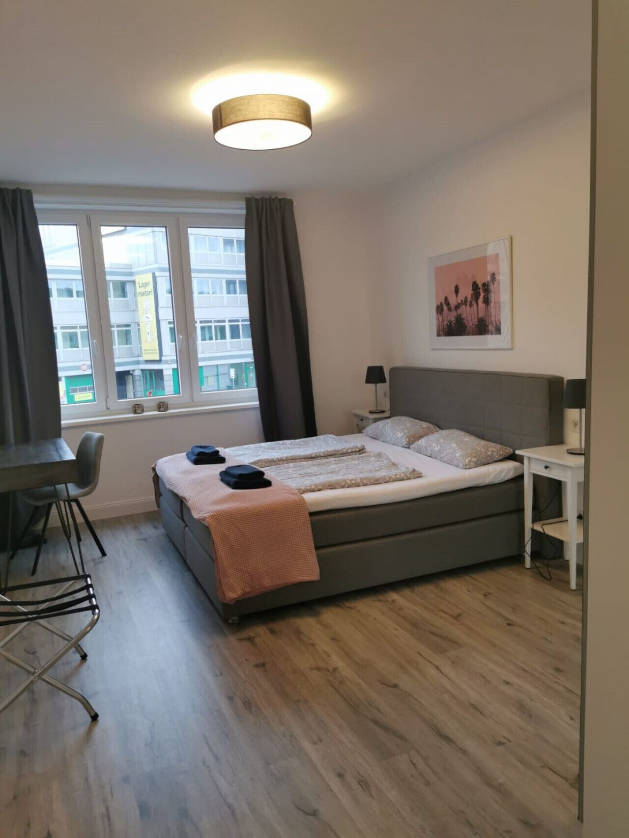 Un dormitorio con cama, escritorio, silla, lámpara y ventana con cortinas.