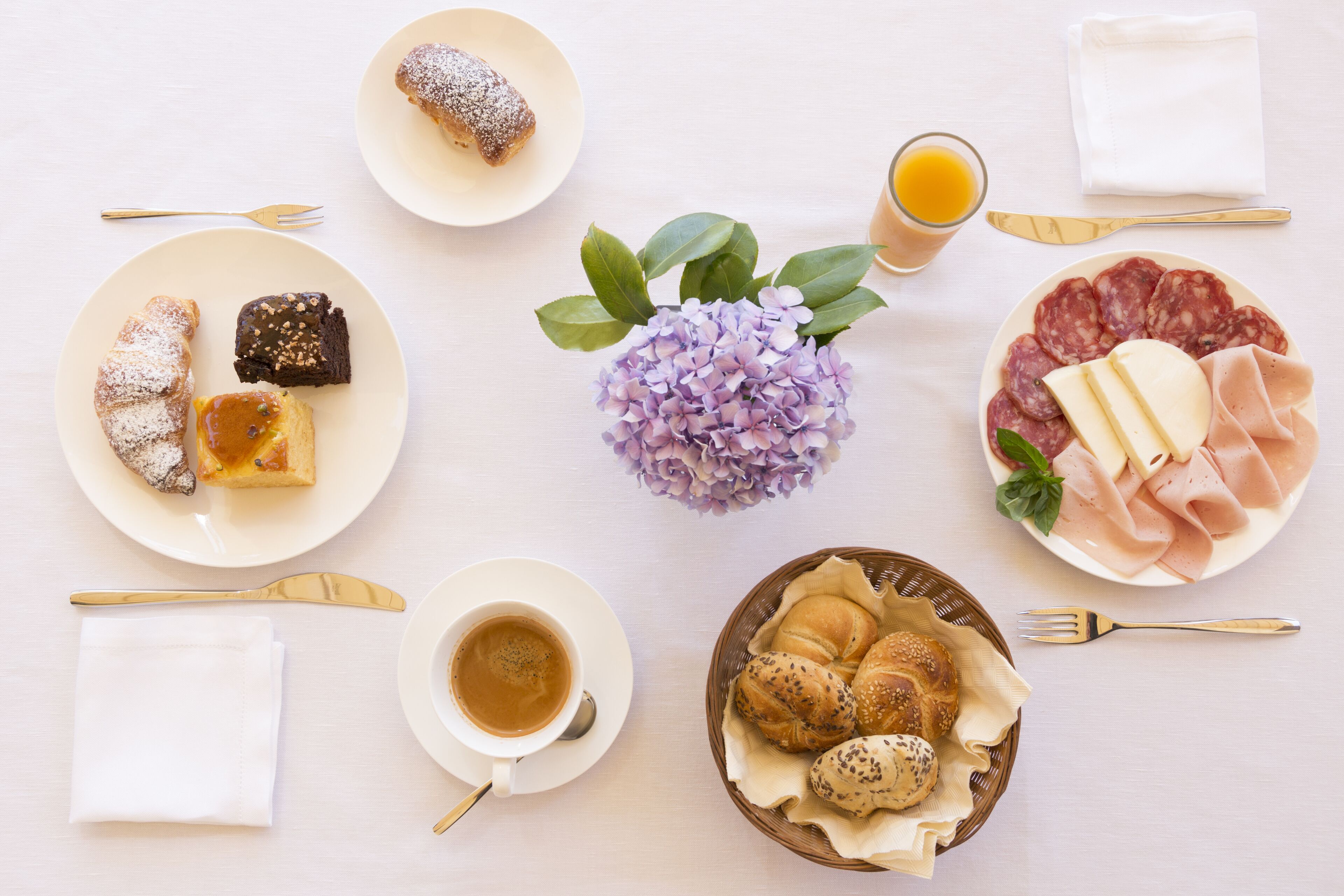 Un desayuno con platos de pasteles, carnes y una taza de café.