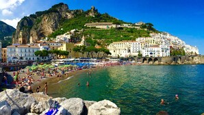 A coastal town with a rocky shoreline, a beach with umbrellas, and a historic hilltop building. - Hotel Zì 'Ntonio (Scala)