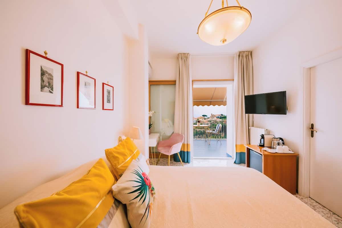Una habitación de hotel con cama, televisión, balcón con vistas y cuadros en la pared.
