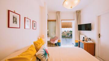 A hotel room with a bed, a TV, a balcony with a view, and framed pictures on the wall.