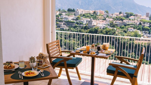 A balcony with a table set for breakfast, overlooking a mountainous town. - Hotel Zì 'Ntonio (Scala)
