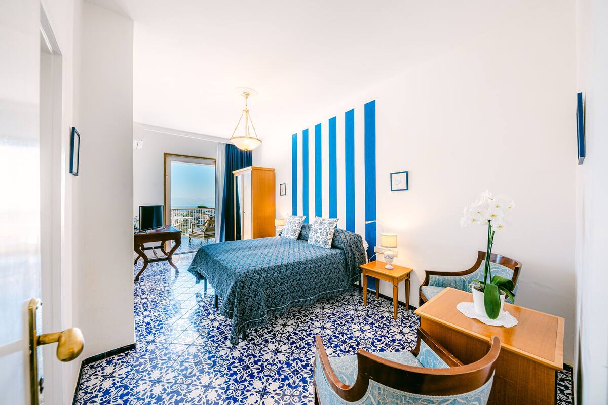 Una habitación de hotel con cama, escritorio, silla, una mesita y una planta en maceta.