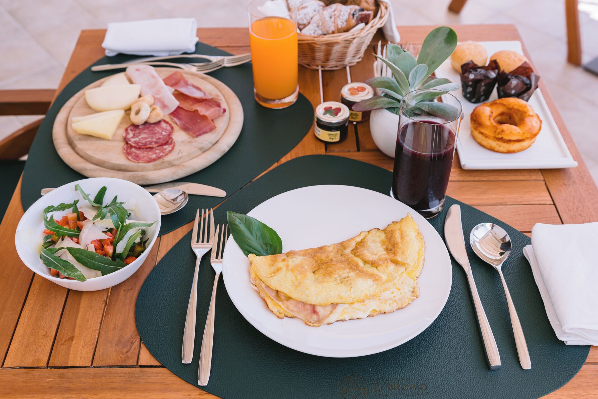 A breakfast setting with a plate of omelette, a bowl of salad, and a plate of assorted meats and cheeses.
